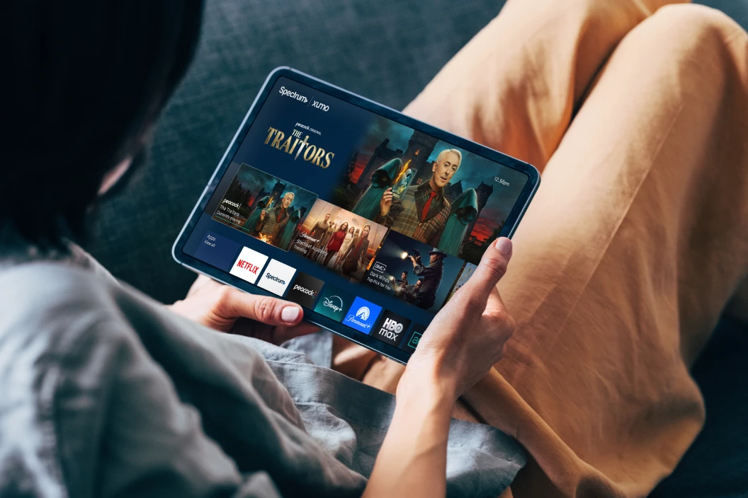 Person holding a tablet displaying a streaming app interface with 'The Traitors' show and app icons including Netflix, Disney+, and others.