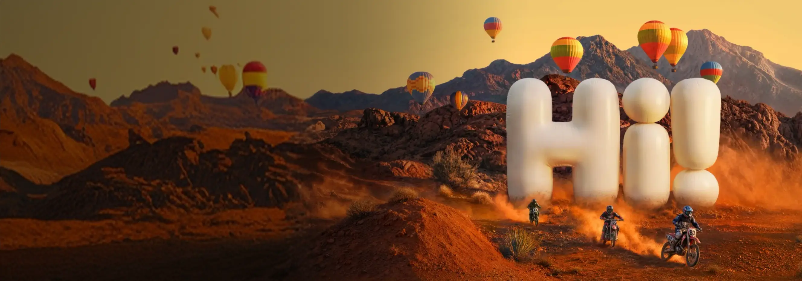 Dirt bike riders climbing a desert trail away from large inflatable-style letters spelling 'Hi!', with colorful hot air balloons floating over rocky mountains.